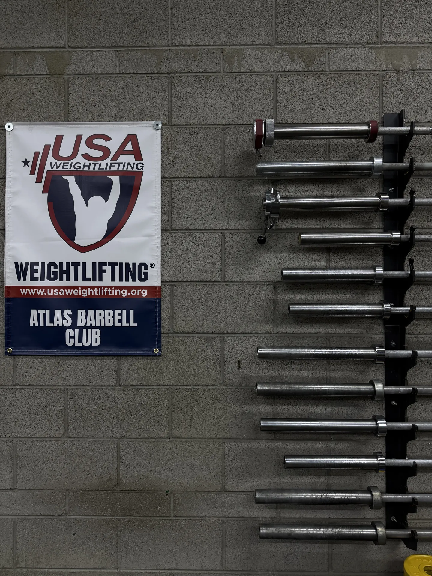 Atlas Barbell Club and USA Weightlifting banners beside the Olympic bar storage